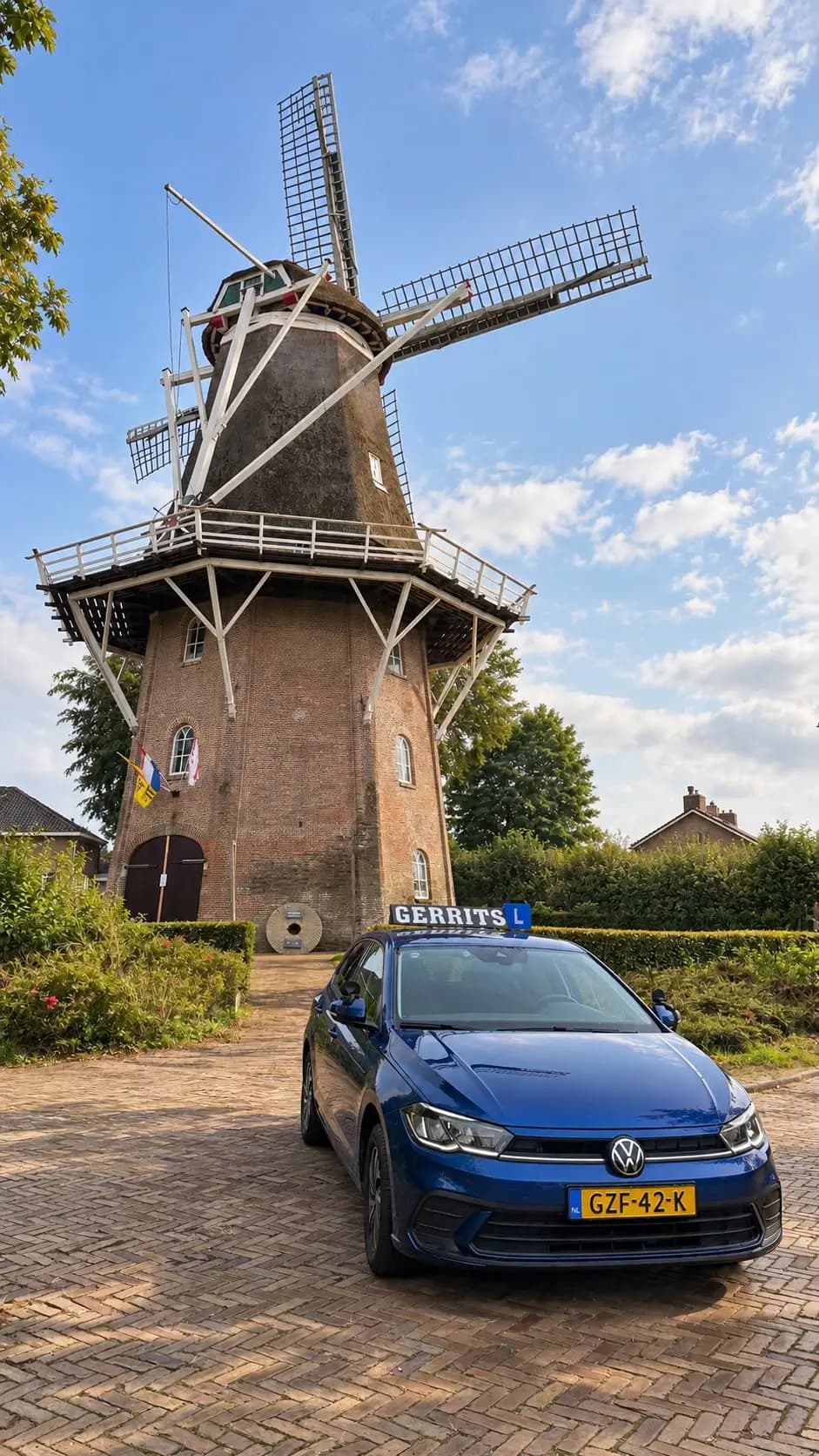 Blauwe Volkswagen Polo schakelauto met lesbord op het dak, vooraanzicht bij de molen