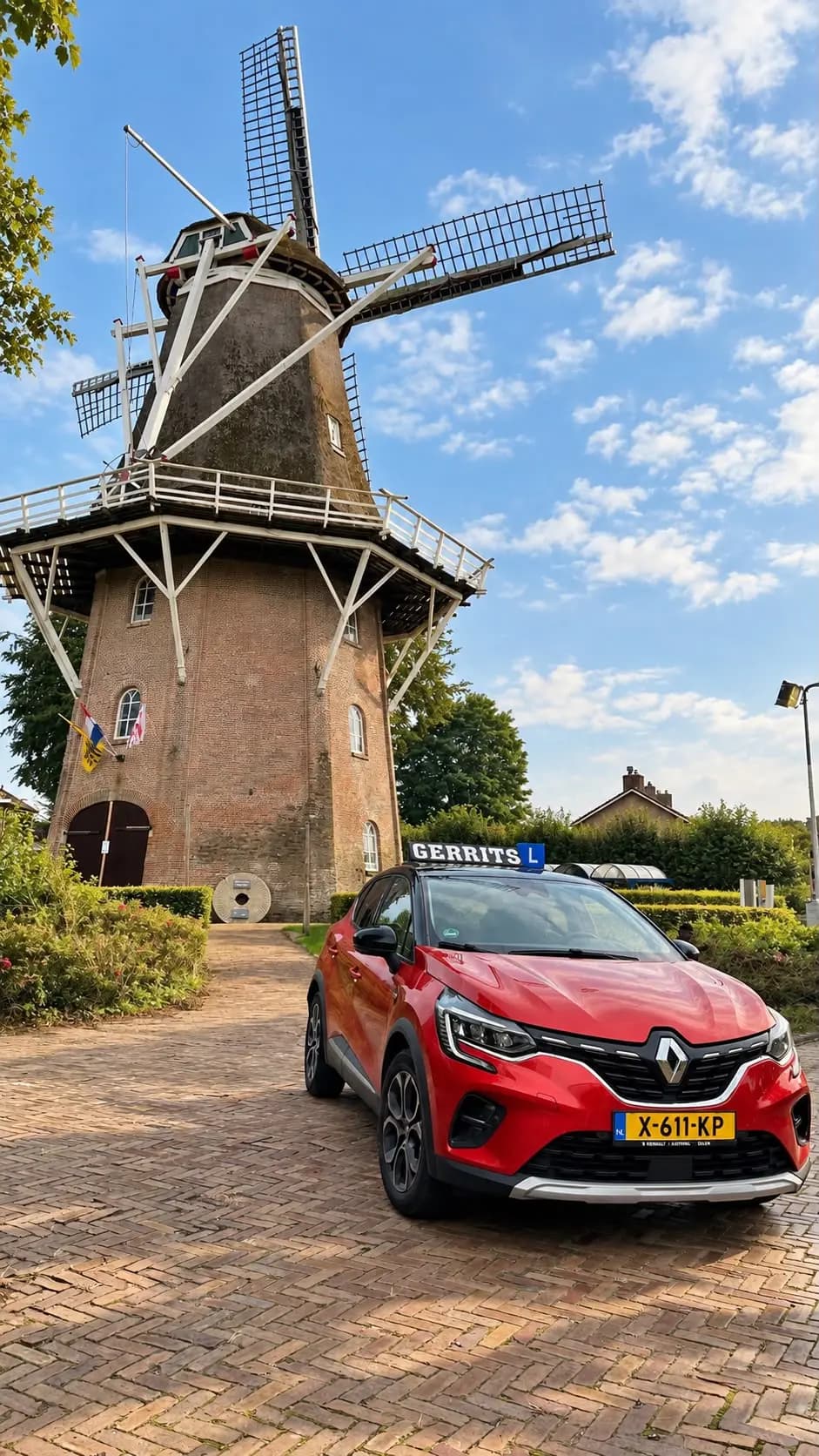 Rode Renault Captur automaat met lesbord op het dak, vooraanzicht bij de molen